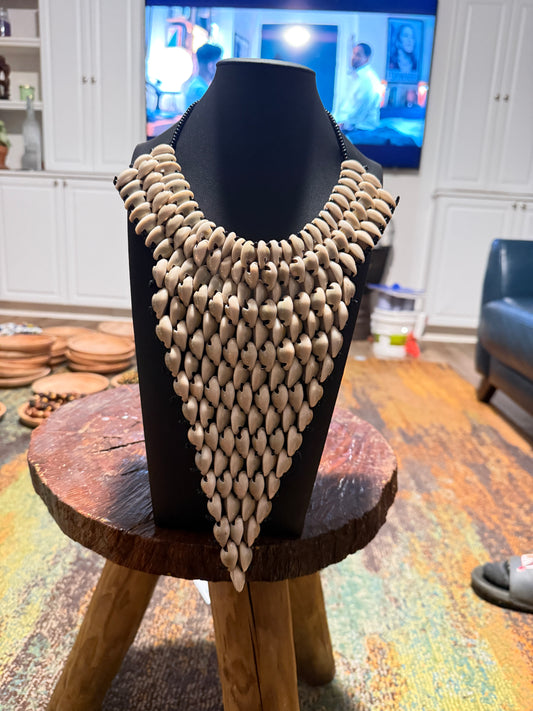 cowrie shell necklace on a black mannequin against a blurred green leafy background
