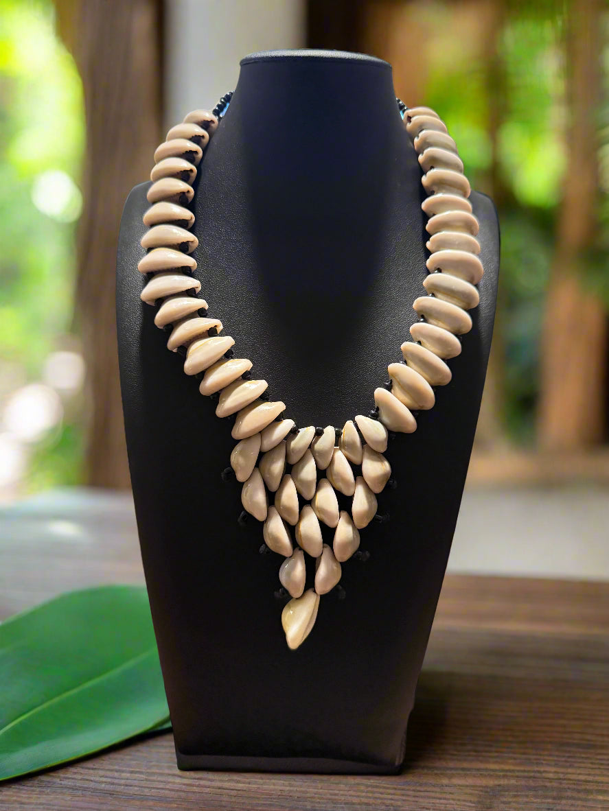 cowrie shell Necklace on a black stand against a blurred natural background