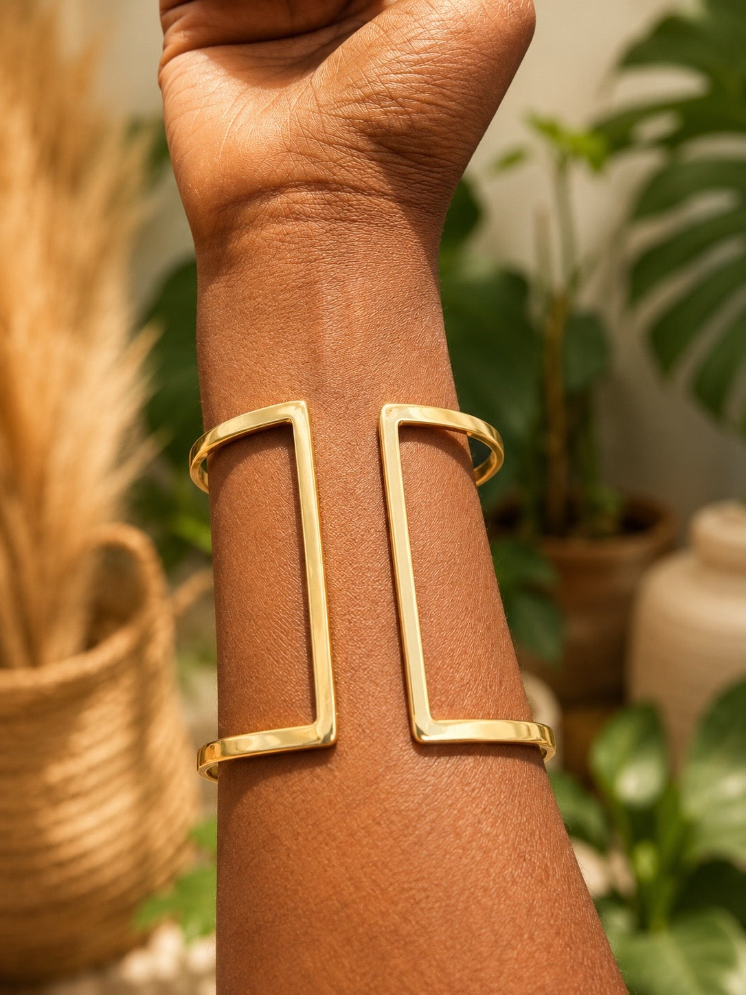 back of a brass bracelet on a wrist with a blurred indoor plant background