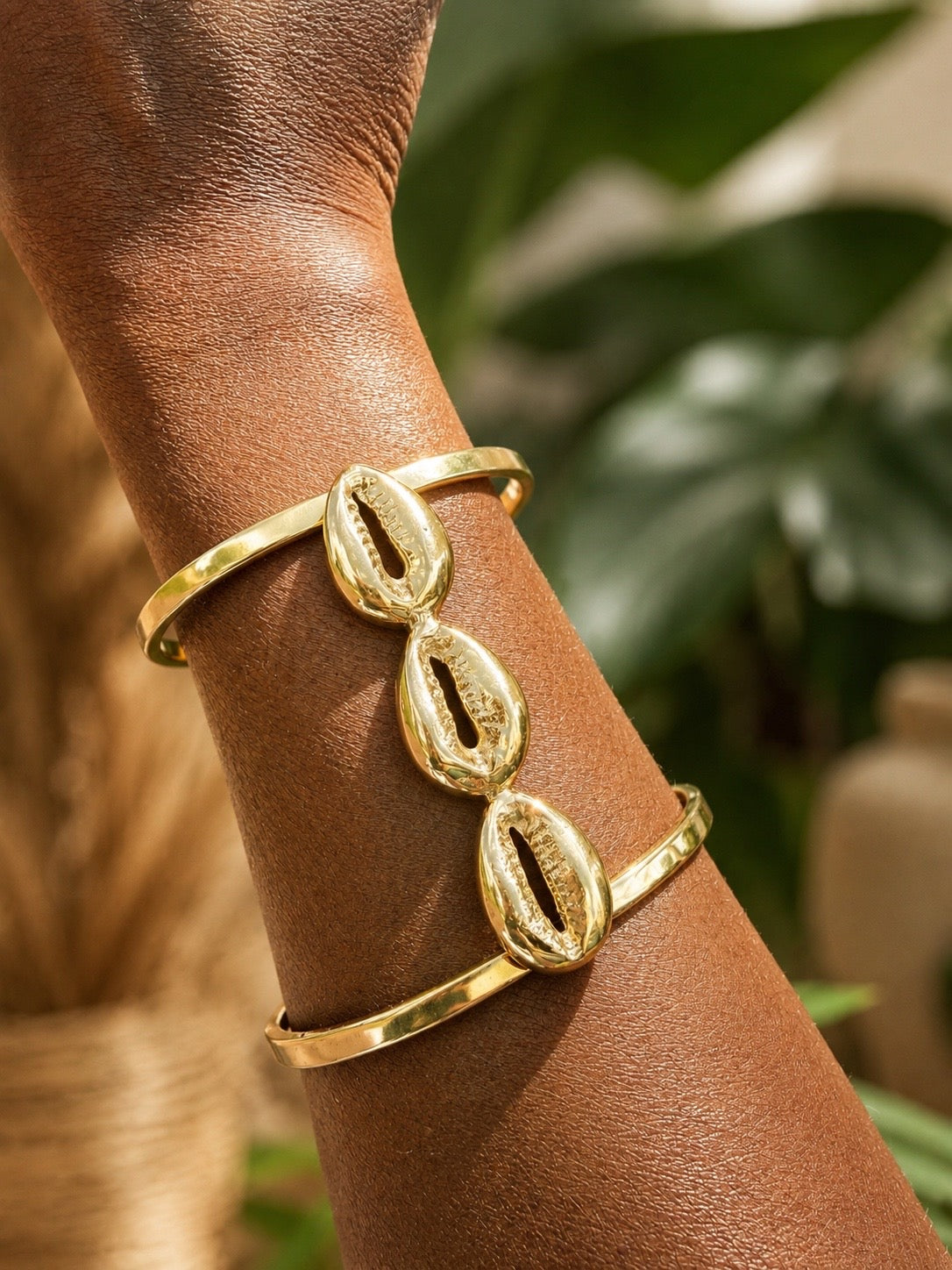 brass cowrie shell bracelet on a wrist with a blurred natural background