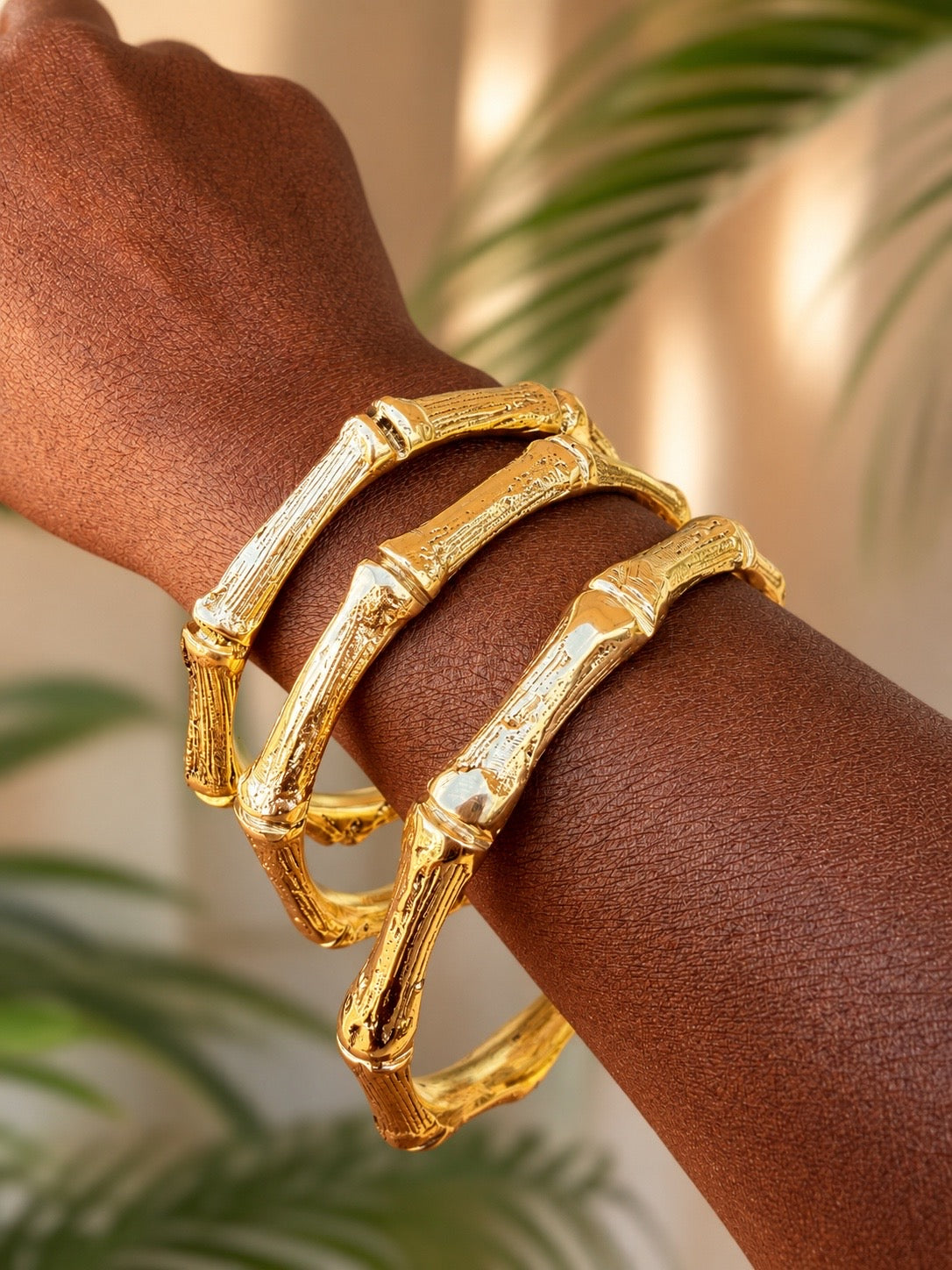 brass bamboo-style bracelet on a wrist with a blurred green leafy background
