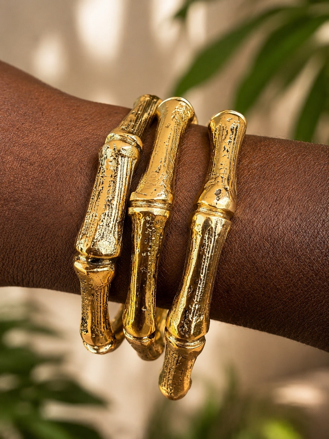 brass bamboo-style bracelets on a wrist with a blurred green leafy background