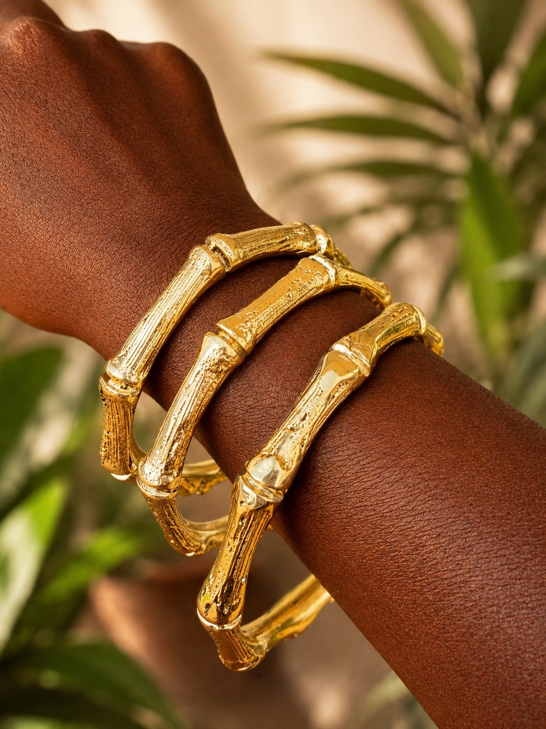 brass bamboo-style bracelets on a wrist with a blurred green leafy background