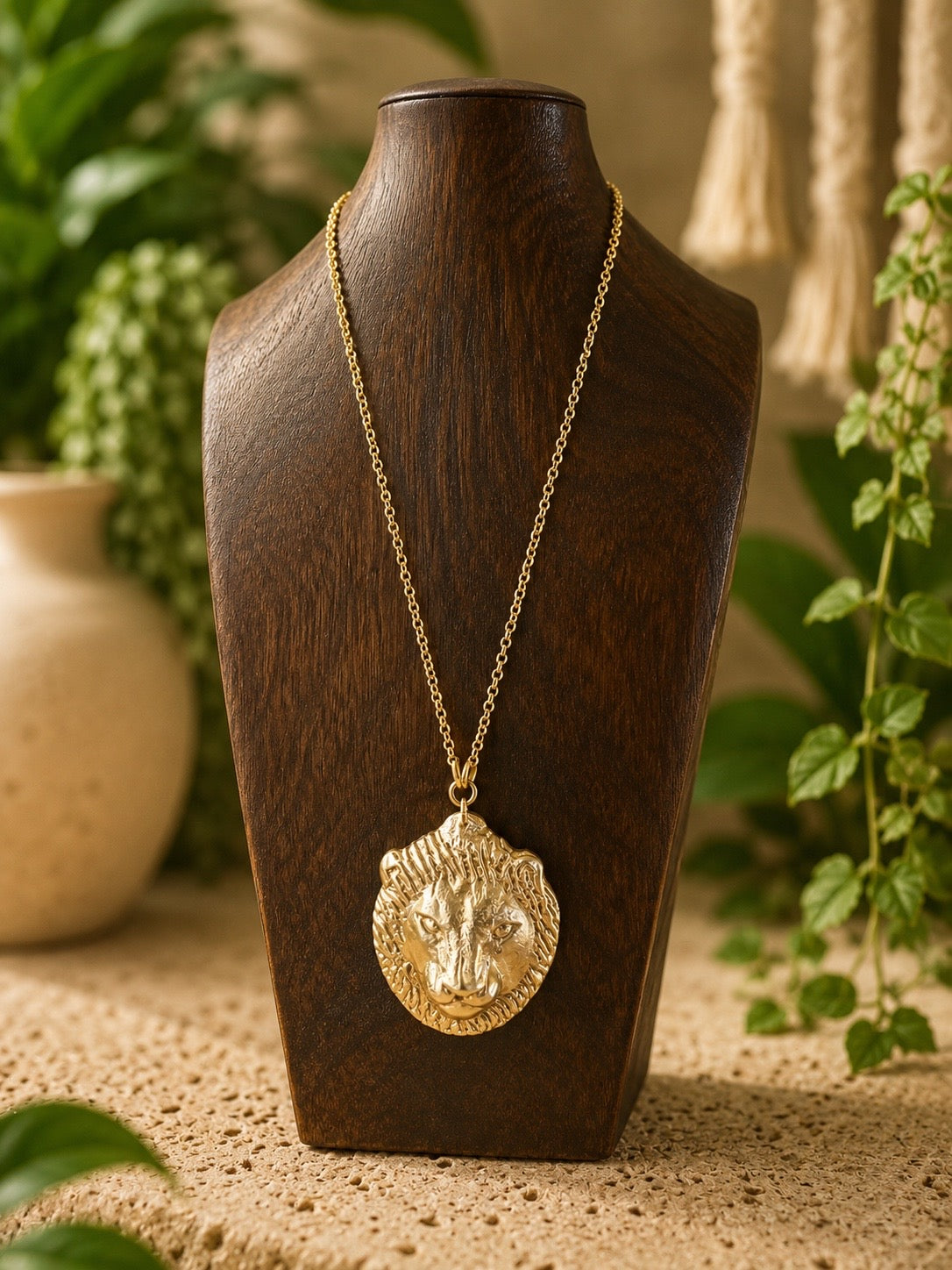 brass lion head pendent on a brass chain on a wooden bust  with a blurred plant background