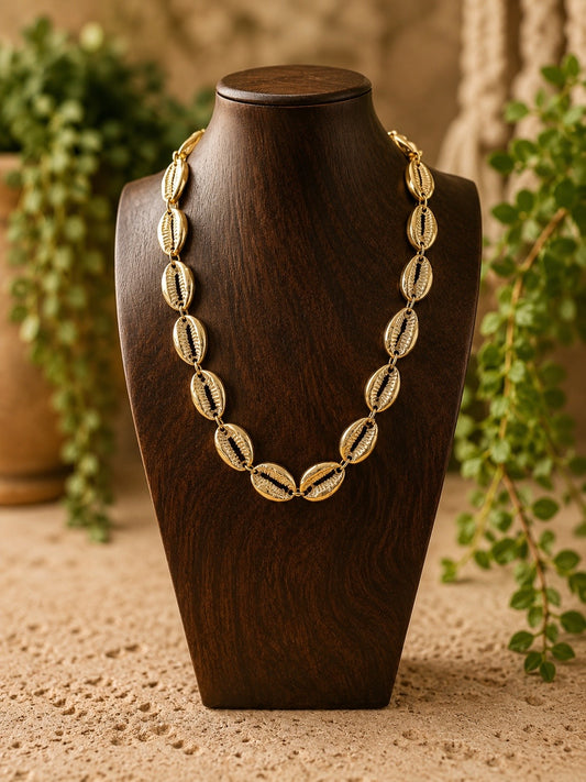 brass cowrie shell necklace on a wooden bust  with a blurred plant background