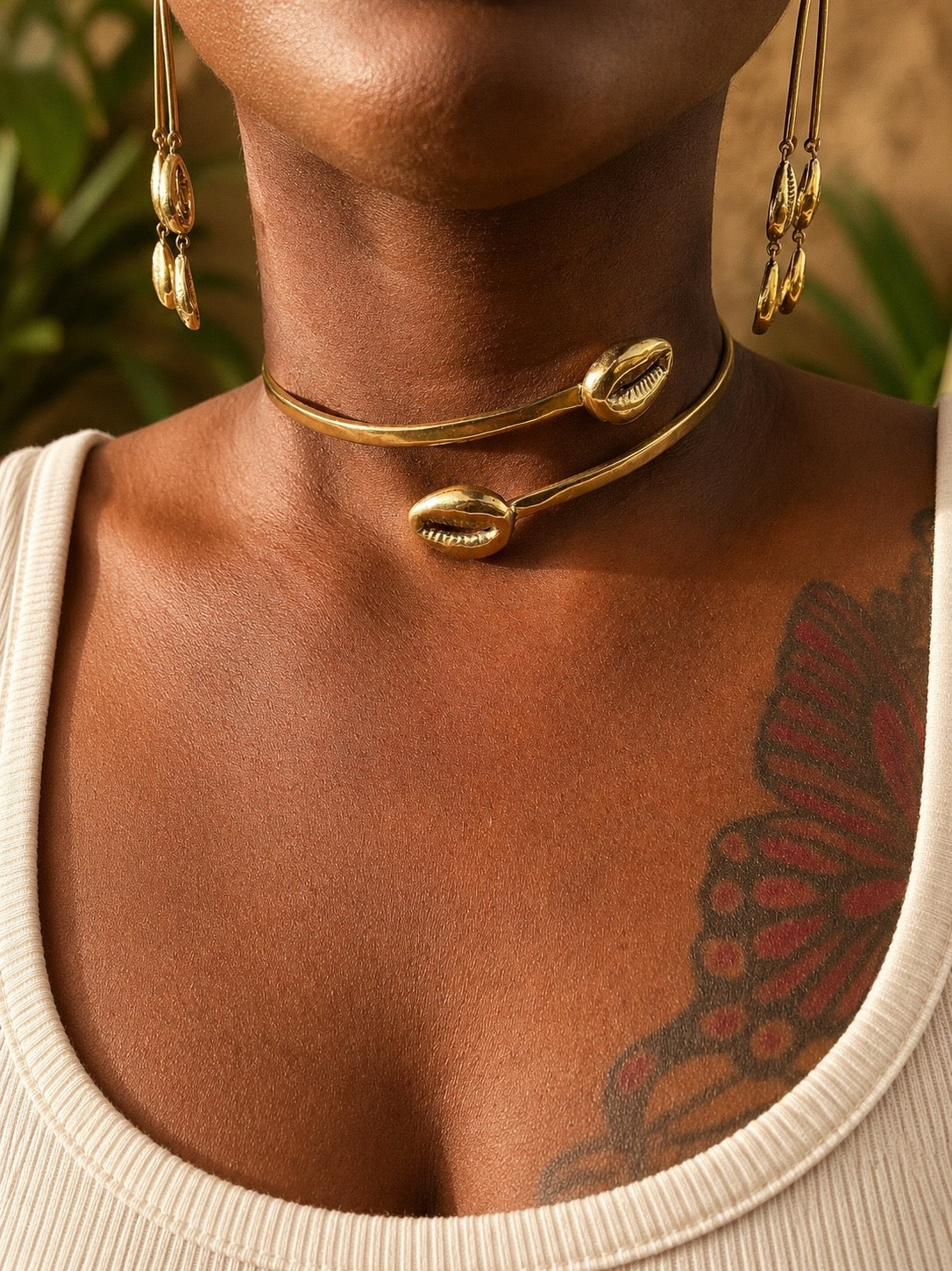 Close-up of a person wearing brass cowrie shell necklaces and earrings with a blurred background