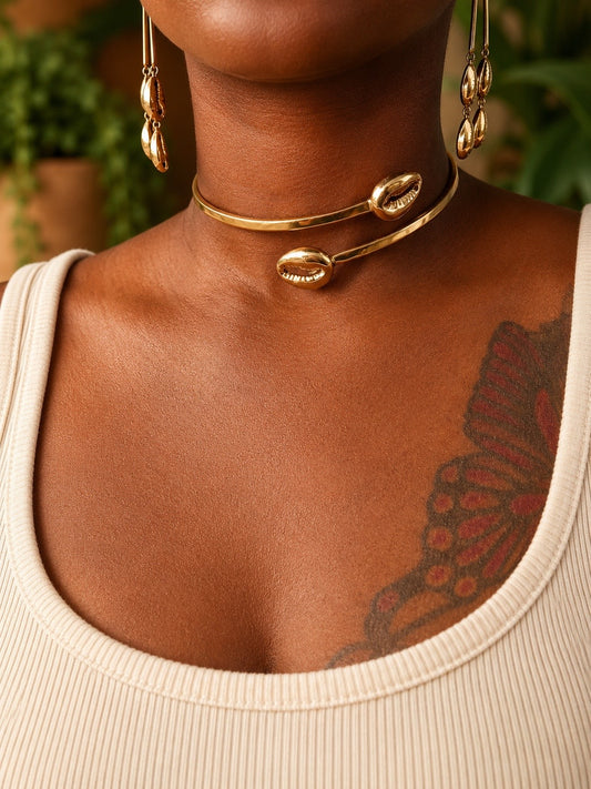 Close-up of a person wearing brass cowrie shell necklaces and earrings with a blurred green background