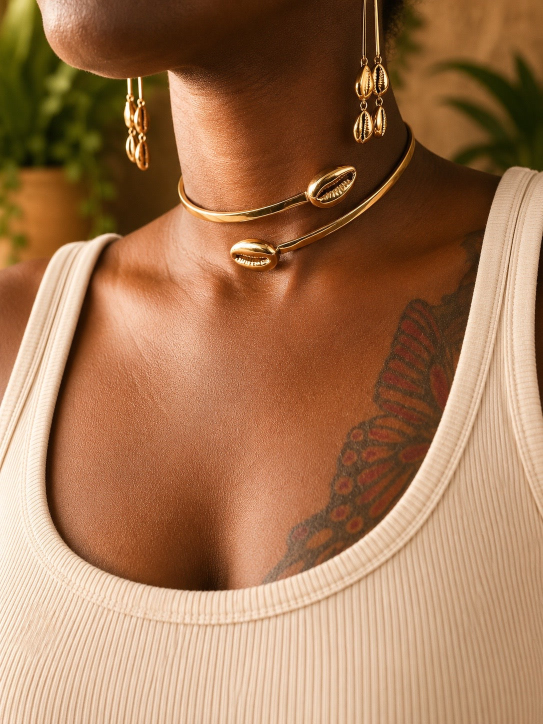 Close-up of a person wearing brass cowrie shell necklaces and earrings with a neutral background