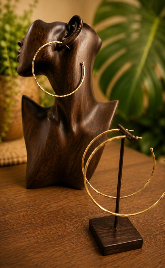 brass hoop earrings on a wooden stand with a wooden bust and green foliage in the background