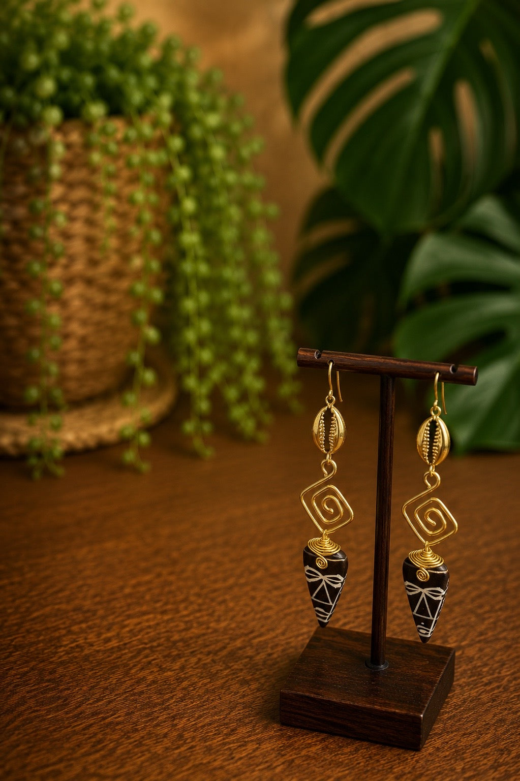 brass and bone cowrie shell earrings on a wooden bust and stand with a blurred plant background
