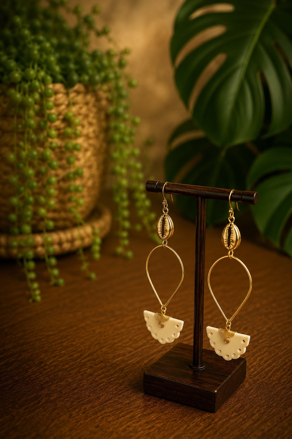 brass and bone cowrie shell earrings on a wooden bust and stand with a blurred plant background
